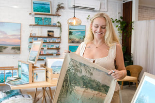 Artist Sharni Montgomery, standing in her studio in front of her landscape art.