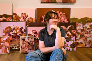 Artist Kelly Fontanarosa wears jeans and a black t-shirt, and sits in front of an array of her abstract still life artworks.