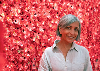 Photographic artist Reshmi Sharma smiles while standing in front of a wall covered in red flowers