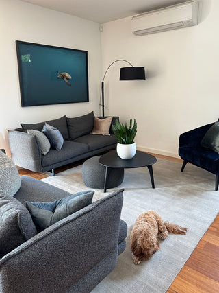 A large scale print by Liam Lynch showing a turtle gliding through a blue ocean sits on a wall above a grey couch.