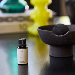 Small bottle of Red Santal essential oil on a reflective surface with blurred background