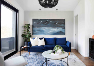 Image of a modern living room with a blue sofa, white cushions, and a large abstract painting on the wall, curated with our professional trade services and art consultations.